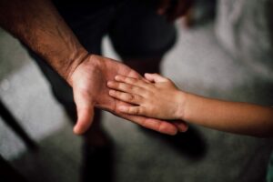 Mano de adulto junto a una mano de niño/a, simbolizando un padre con su hijo/a