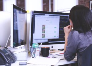 Imagen de una mujer trabajando frente a dos pantallas de computador para aludir al desgaste laboral o burnout.