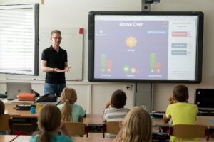 Imagen de un profesor explicando en una clase a niños y niñas para representar al Día Internacional de la Educación.