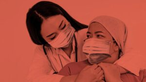 Imagen de la OPS para el Día Mundial contra el Cáncer. Aparece una doctora abrazando a una paciente con mascarilla. La imagen además lleva un filtro rojo.