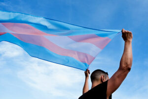 Persona flameando la bandera trans. Imagen utilizada para aludir al Día de la Visibilidad Trans.